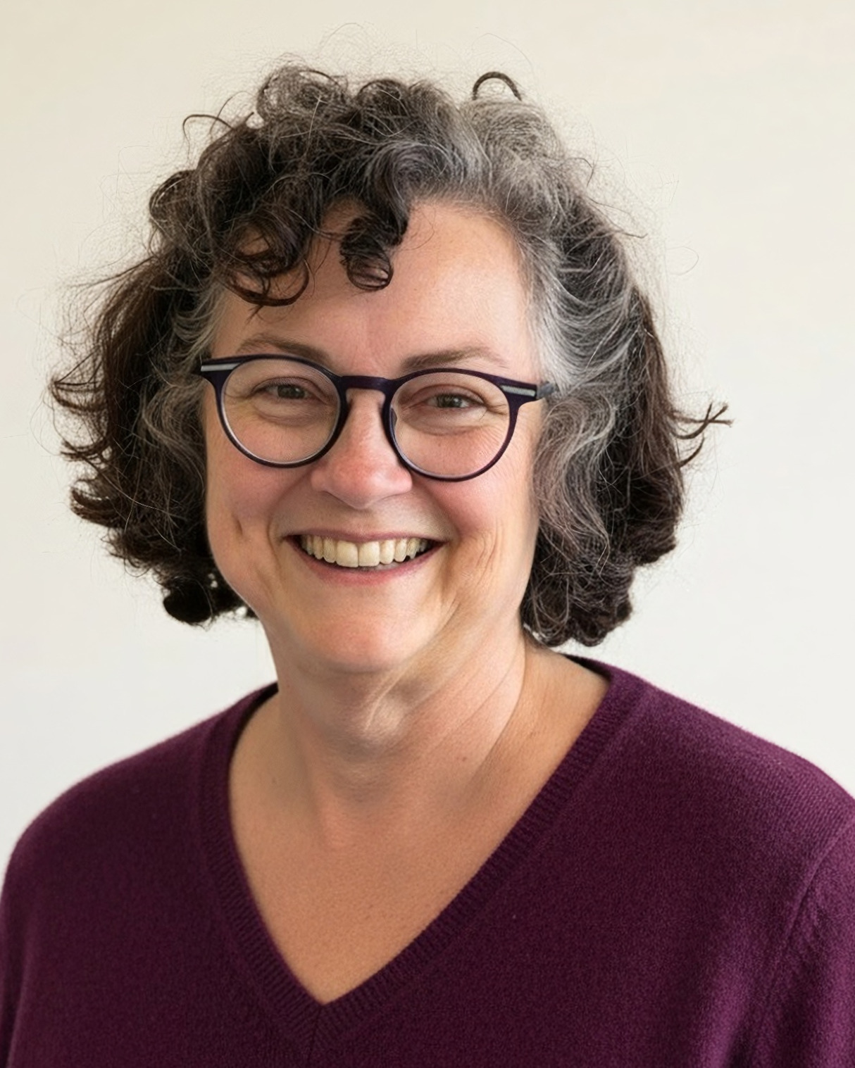 Smiling white woman with graying brown hair, glasses and a dimple